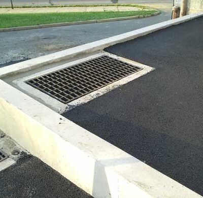 A picture of concrete curbing with a concrete drain set in asphalt