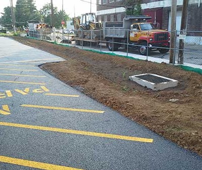 Picture of the side of the larger parking lot, showing the top soil that was spread, the drain placed, and the sidewalk installed.
